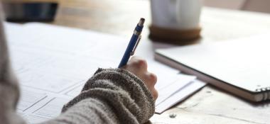 Person with a pen at a desk with papers and an open notebook